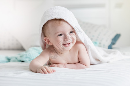 穿着毛巾的可爱笑婴儿肖像洗完澡后躺在床上图片
