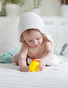 穿着蒙面毛巾的快乐小男孩肖像在洗完澡后床上玩黄色橡皮鸭背景图片