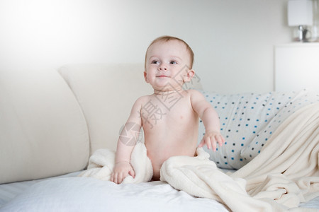 可爱笑的婴儿男孩穿着尿布坐在床上带白单穿着图片