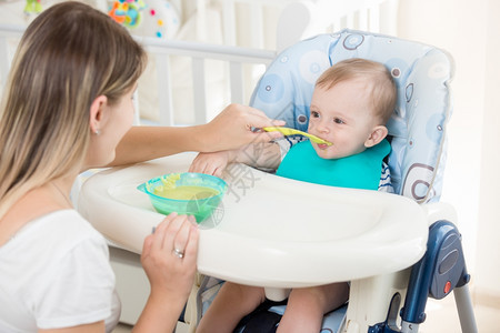 婴儿男孩坐在高椅子上吃粥的肖像图片