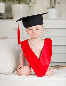穿着毕业帽子的可爱小男孩肖像和坐在床上的红领图片
