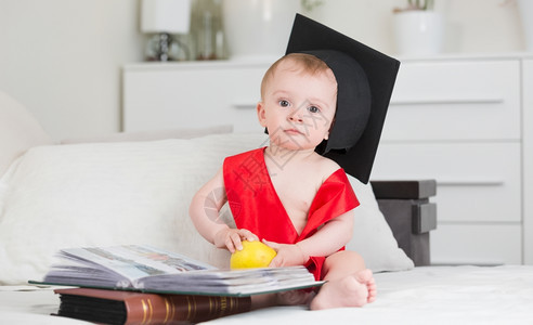 10个月大身着毕业帽子的男婴坐在沙发上带着书籍图片