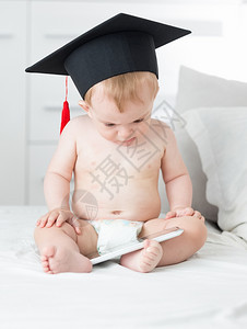 10个月大的婴儿男孩穿着尿布佩毕业帽并使用平板电脑c图片