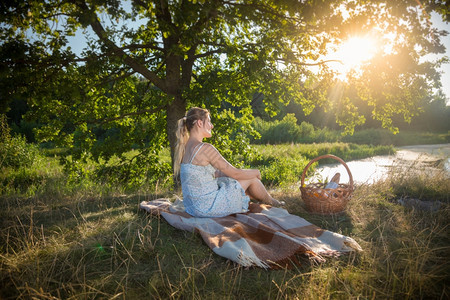 穿着裙子的漂亮女人在树下毛毯上放松看着日落图片