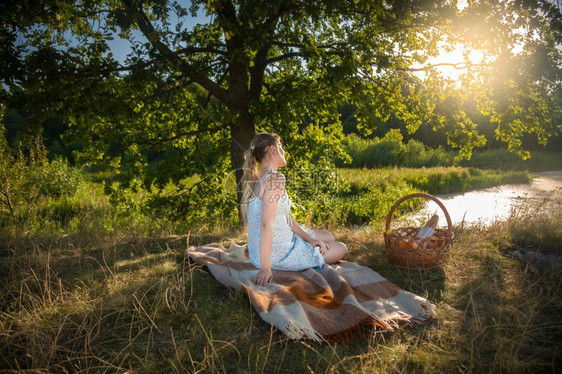 美丽的年轻女士坐在田野的大树下看着日落图片