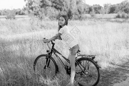 美丽的少女在草地骑自行车的黑白画面图片