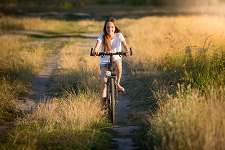 美丽的笑女孩在日落时草地上骑自行车图片