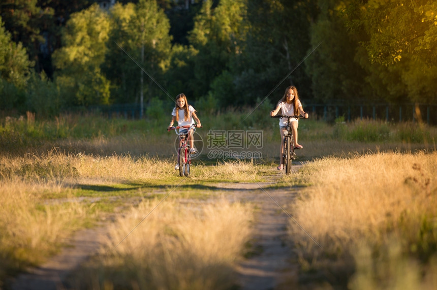 两名少女在日落时草地上骑自行车的画面图片