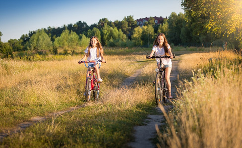 两个美丽的女孩在阳光明媚的天骑着自行车在草地上骑着自行车图片