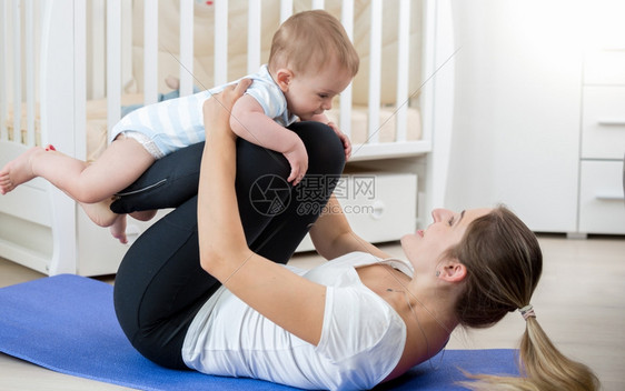 美丽的微笑女士与婴儿在客厅做瑜伽锻炼图片