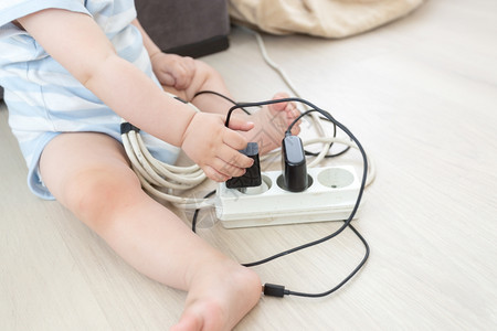 婴儿男孩从电源扩展线抽取缆的近照片高清图片