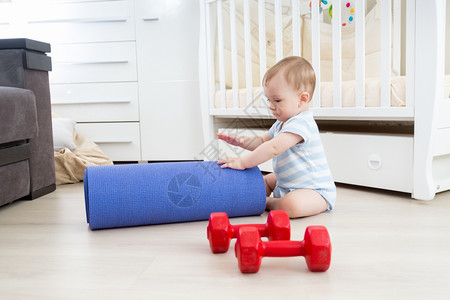 与健身垫和哑铃一起在地板上玩耍的可爱笑婴儿图片