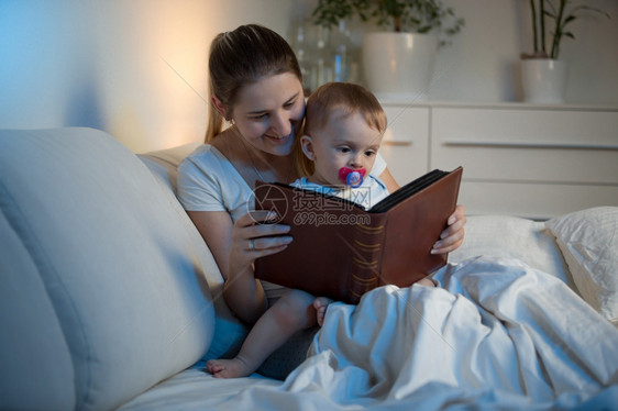 年轻母亲晚上在床上给婴儿看书图片