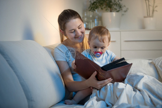 年轻母亲晚上在床上给婴儿看书图片
