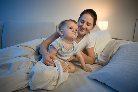可爱的男婴和他母亲深夜上床睡觉的肖像图片