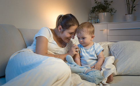 美丽的微笑母亲肖像躺在床上睡觉前和婴儿玩耍图片