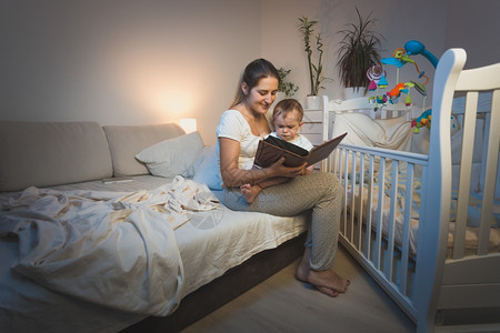 美丽的母亲肖像抱着小男孩跪在膝上睡觉前读一本书图片