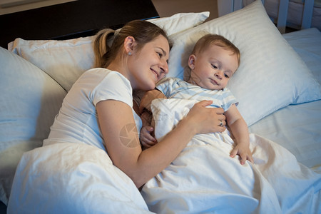 快乐的妈微笑拥抱她可爱的宝晚上在床图片