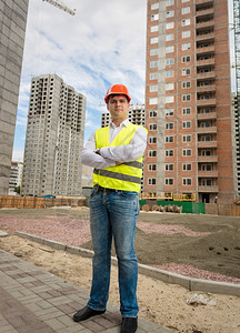 在建筑工地站立的戴头盔和安全背心的有自信工人微笑图片
