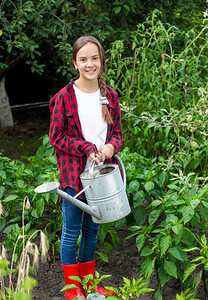 穿着红色橡胶靴子在花园浇蔬菜的快乐少女图片