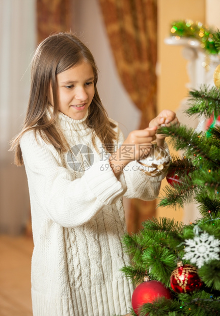 穿着羊毛衣在家里装饰圣诞树的少女快乐肖像图片