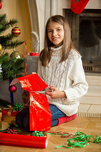 快乐女孩坐在壁炉上包着圣诞礼物的肖像图片