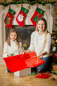 快乐的少女和母亲肖像坐在壁炉里包着圣诞礼物图片