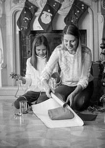 女儿在壁炉上包装圣诞礼物的年轻快乐母亲黑白画像图片