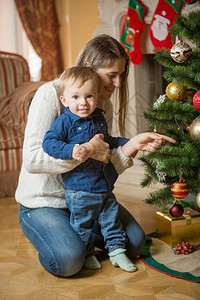 快乐的母亲和十个月大的小孩男在家里装饰圣诞树图片
