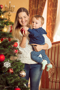 快乐的年轻女人肖像带着她儿子的宝装饰圣诞树图片