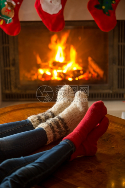 在燃烧的壁炉里暖羊绒袜子中男女双脚的近视图像图片