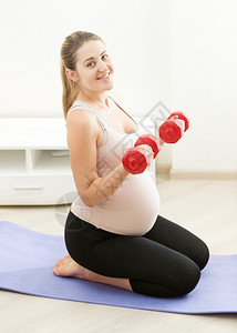 坐在健身垫子上并举重锻炼的年轻孕妇图片