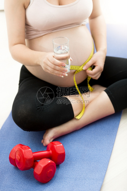 孕妇在健身席和水杯上用测量胶带腹部的孕妇图片