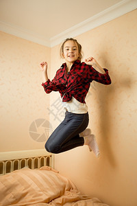 穿着衬衫和牛仔裤的快乐少女在床上跳跃图片