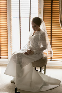 美丽的年轻新娘在酒店房间大窗户对着的椅子上摆姿势图片