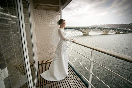 美丽的年轻新娘在阳台上摆姿势看着河流图片