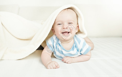 笑得可爱6个月婴儿男孩躺在床毛毯下上图片