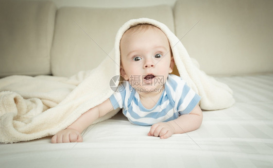 令人惊讶的男孩子有趣肖像看着镜头从毯子下图片