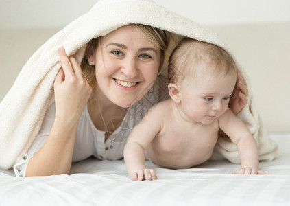 微笑的快乐母亲和婴儿的肖像床盖着毯子图片