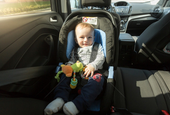 坐在汽车儿童座椅上戴着帽子的可爱笑男孩图片
