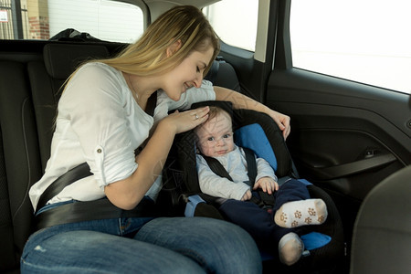 年轻有照护的母亲肖像和她婴儿男孩坐在车后座的上图片
