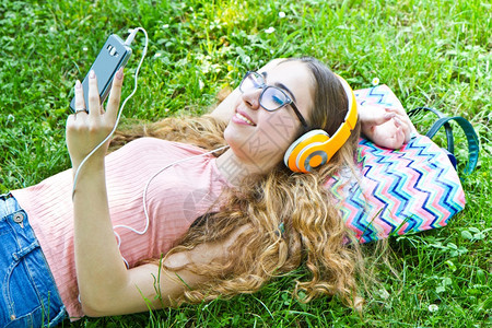美丽的女孩在公园耳机里放松听音乐图片