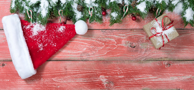 圣诞概念的雪鲜红色木质背景包括圆木枝糖果杖红莓圣诞树帽礼品盒和松果图片