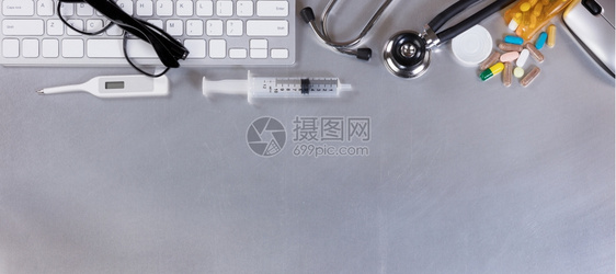 具有计算机键盘听诊器温度计药品老鼠和注射器的不锈钢医生桌子图片
