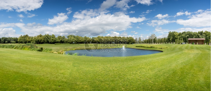 阳光明媚的夏日高尔夫球场和池塘的全景图片
