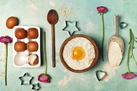 用面粉鸡蛋厨房用具和鲜花烘烤背景在蓝绿色的桌子上图片