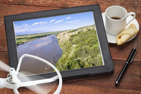 NebraskaSandHills的NiobraraRiverHills浏览数码平板上的空中照片面有无人机螺旋桨和咖啡图片