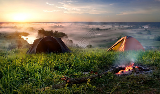 日出时在河附近草原的帐篷和营火图片