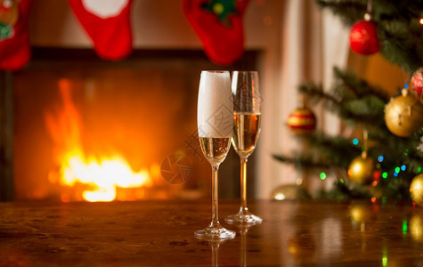 在圣诞树旁边的桌子上装满香槟的两杯子图片