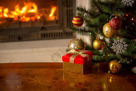 在燃烧的壁炉和圣诞树前面的木制桌上红色礼品盒关闭图像图片